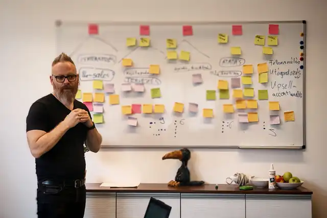 Klein Péter egy cetlikkel teli tábla előtt áll és magyaráz egy workshopon.
